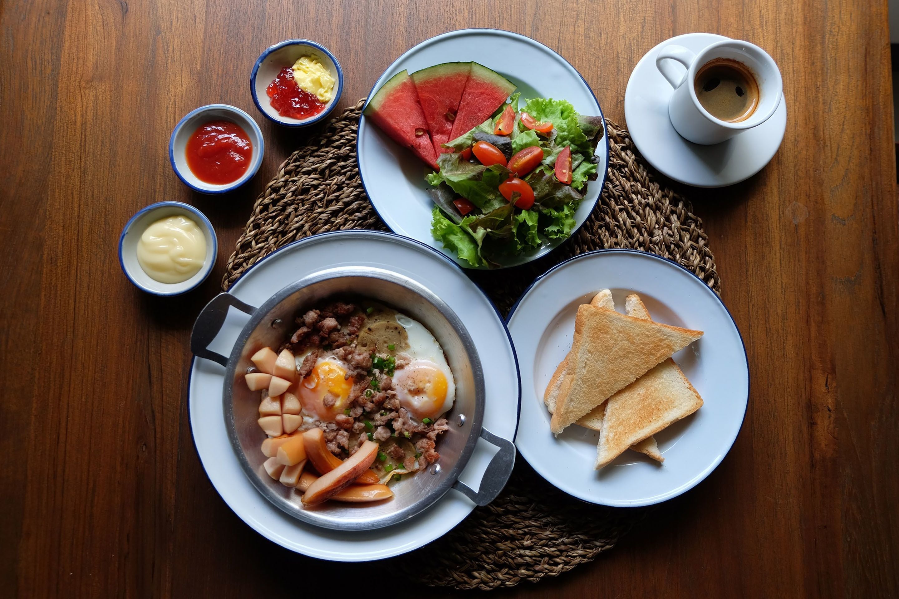 A breakfast setting with a plate of toast, a bowl of soup, a salad, a cup of coffee, and small bowls of condiments.
