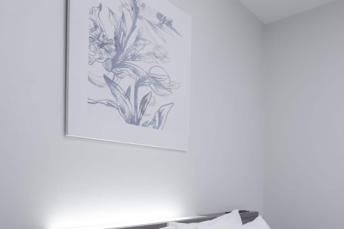 A neatly made bed with white bedding and pillows, a framed floral artwork on the wall, and a modern headboard.
