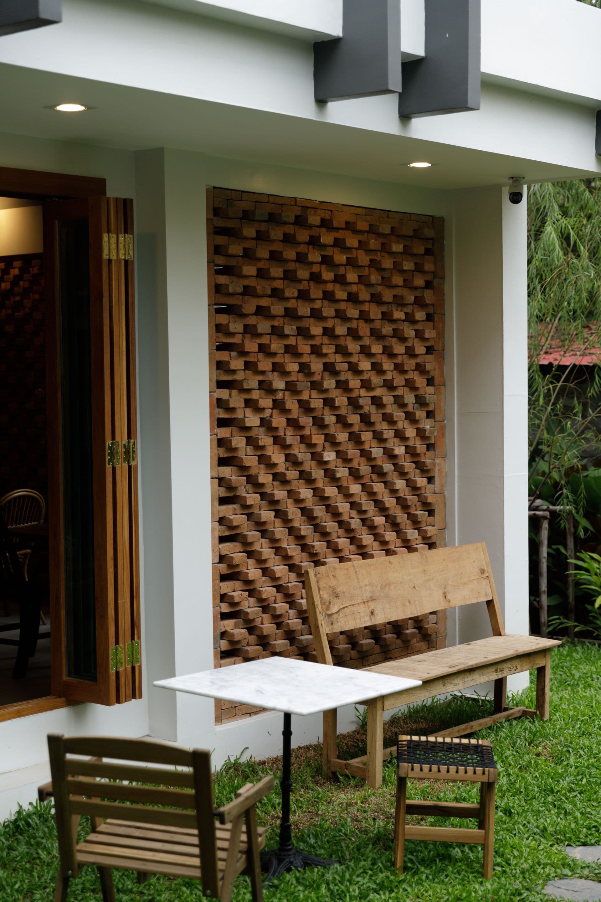 A modern outdoor seating area with a wooden bench and table, surrounded by a brick wall and greenery.