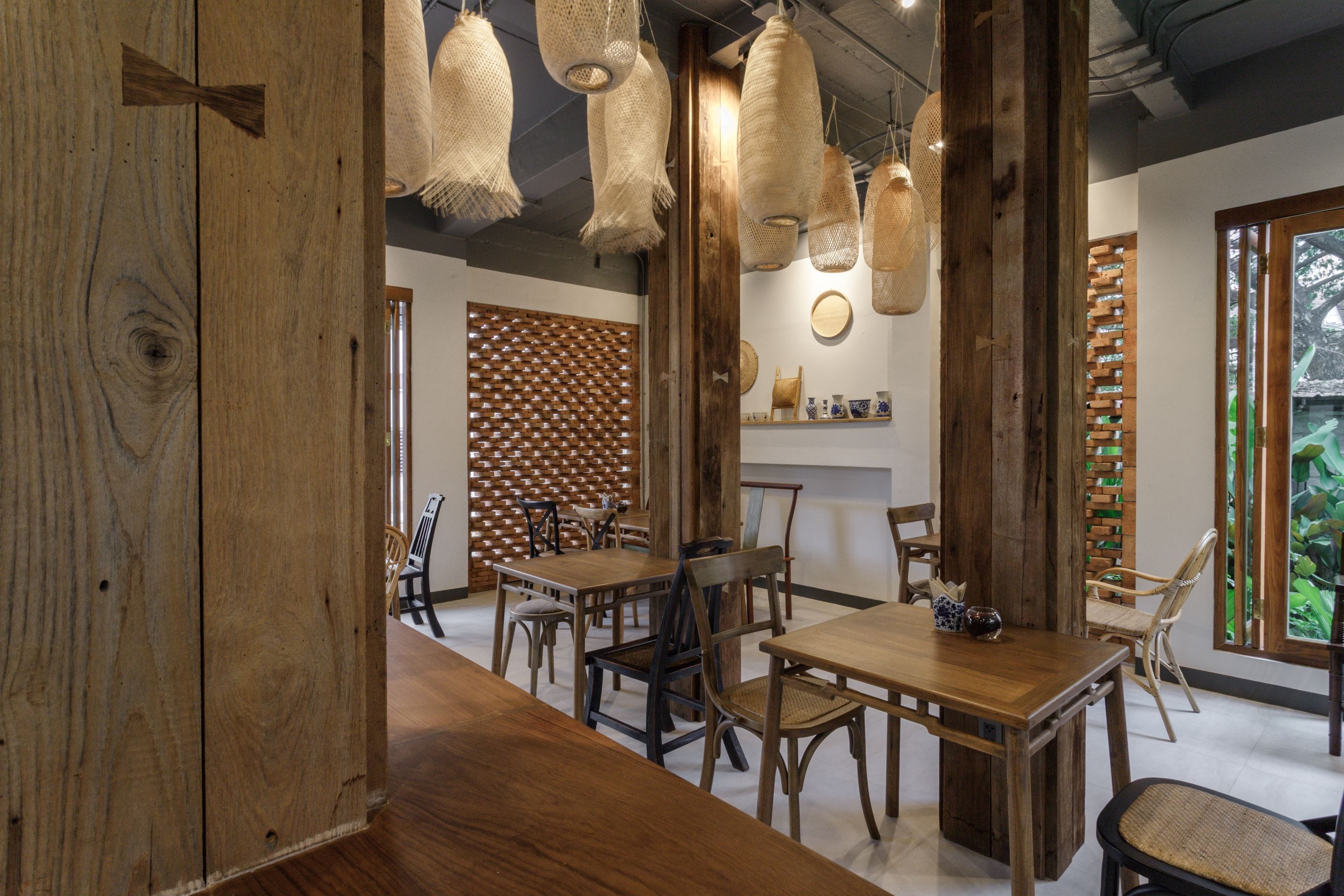 A wooden dining area with tables and chairs, hanging light fixtures, and a wooden partition with a lattice design.