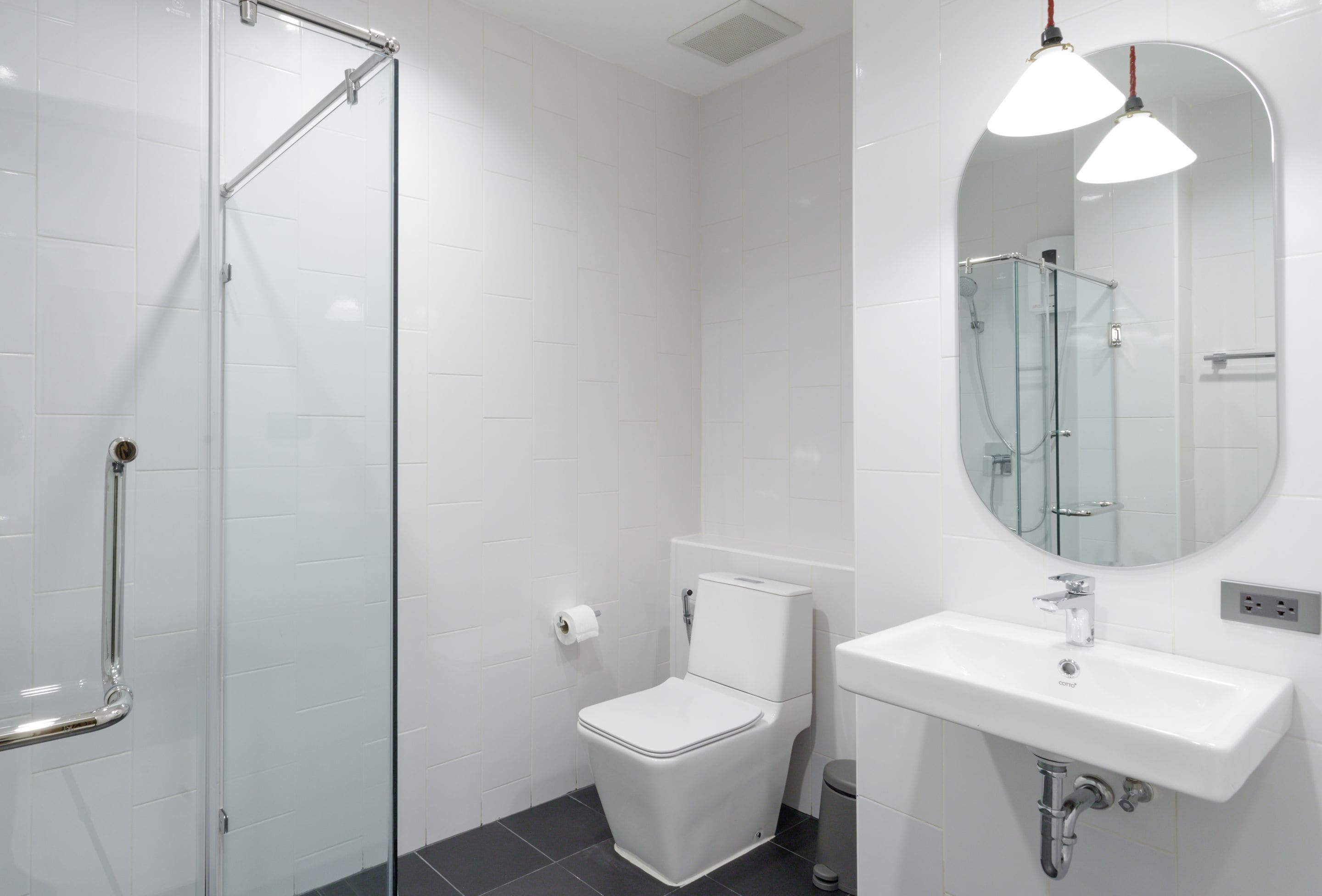 Une salle de bain moderne avec une douche à parois de verre, des toilettes blanches et un lavabo surmonté d’un miroir.
