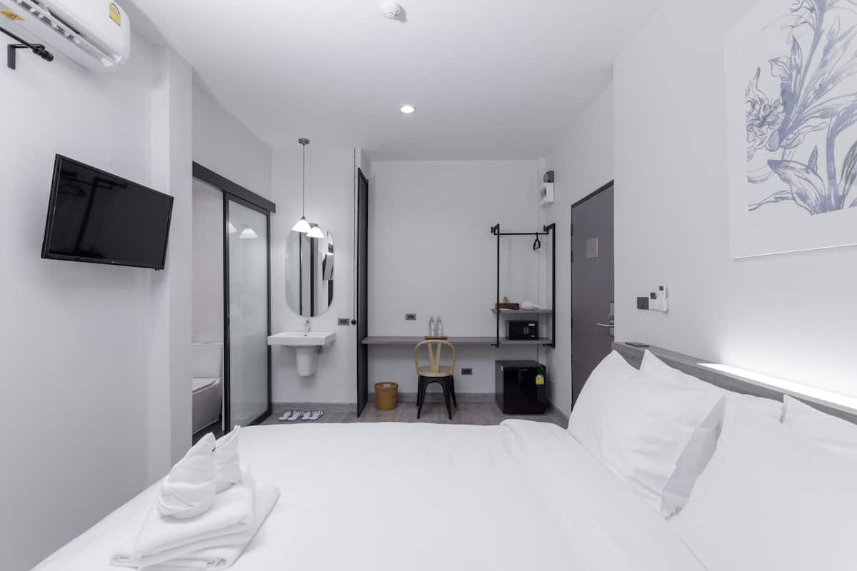 A modern hotel room with a bed, a TV, a sink, and a mirror.