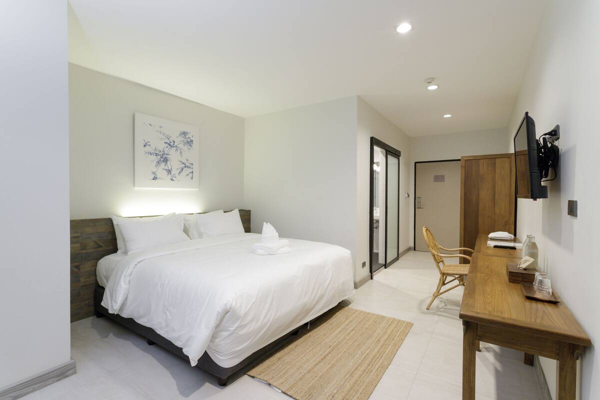 A modern bedroom with a large bed, a wooden desk, and a chair.