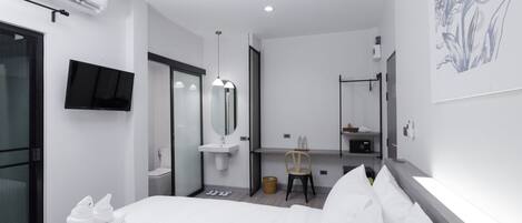 Una habitación de hotel moderna con cama, televisor de pantalla plana, escritorio con silla, espejo y aire acondicionado instalado en la pared.