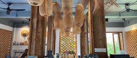 Una habitación con pilares de madera, lámparas colgantes tejidas y diversos objetos decorativos sobre las mesas.
