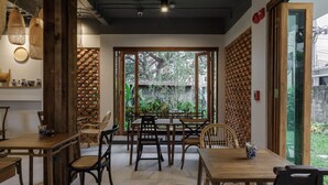 A dining area with wooden tables and chairs, a brick wall, and a view of greenery outside. - The Locals Chiang Mai (Chiang Mai)