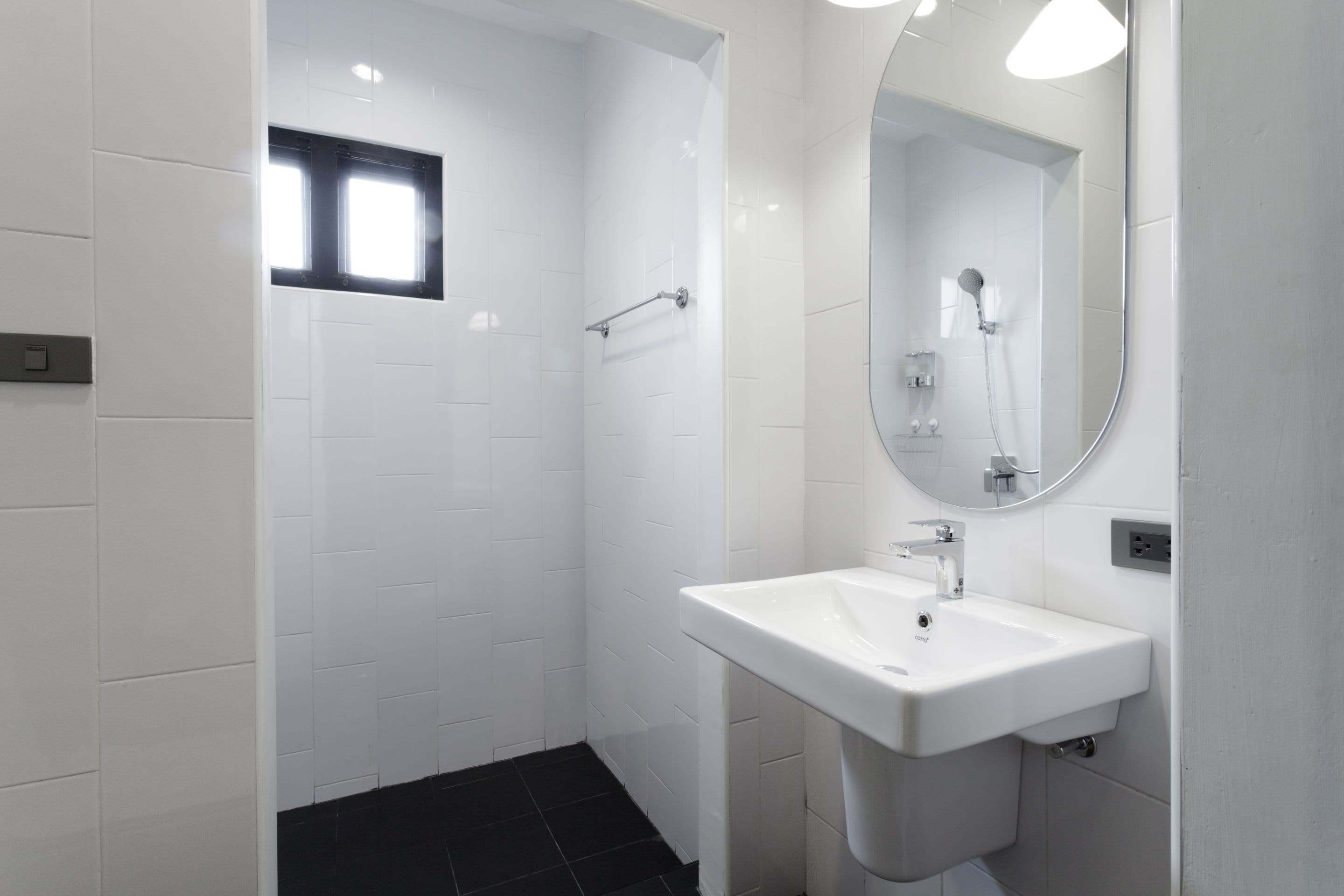 A modern bathroom with a white tiled shower, a sink with a mirror, and a black tiled floor.