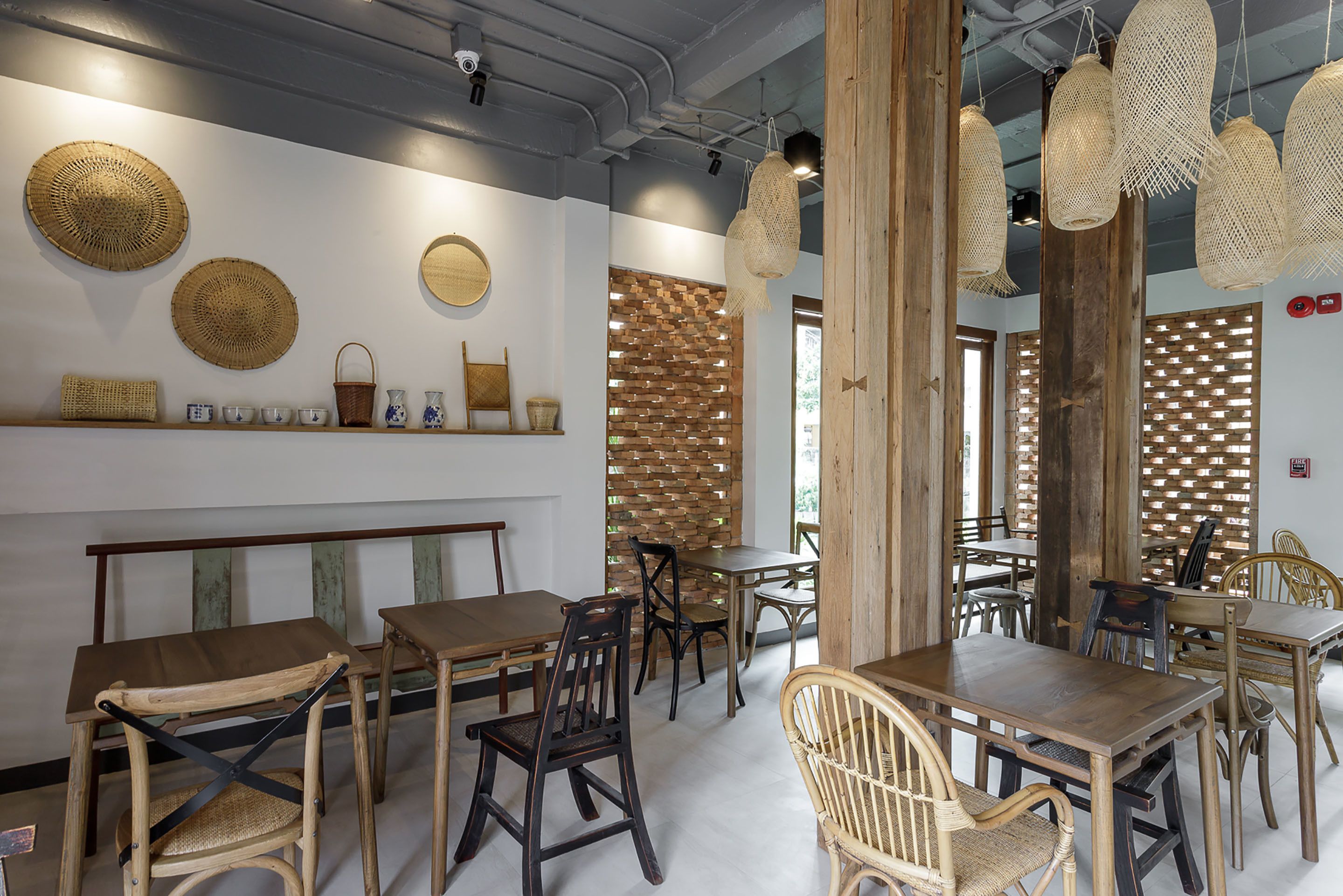 Un comedor con mesas y sillas de madera, cestas tejidas y una pared de ladrillo.