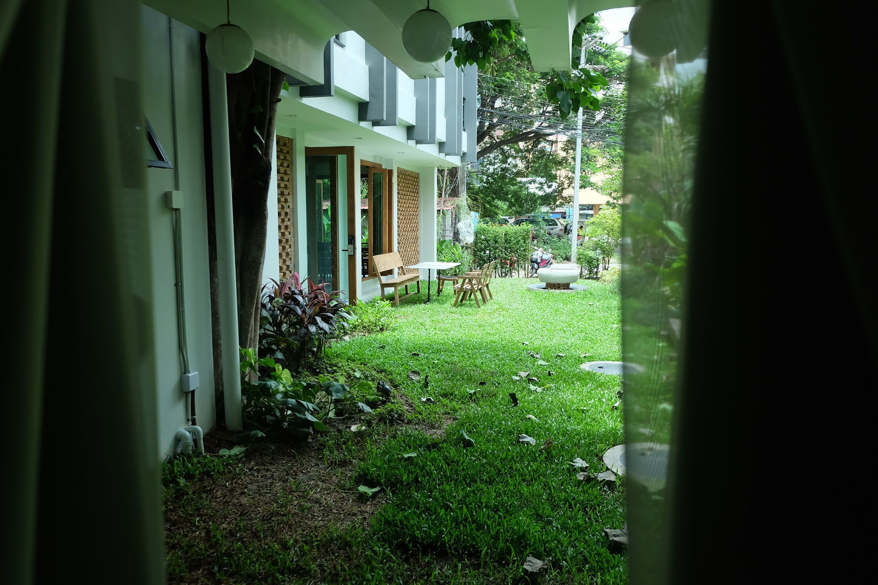 A view of a building with a covered outdoor seating area, a lawn, and a pathway leading to the entrance.