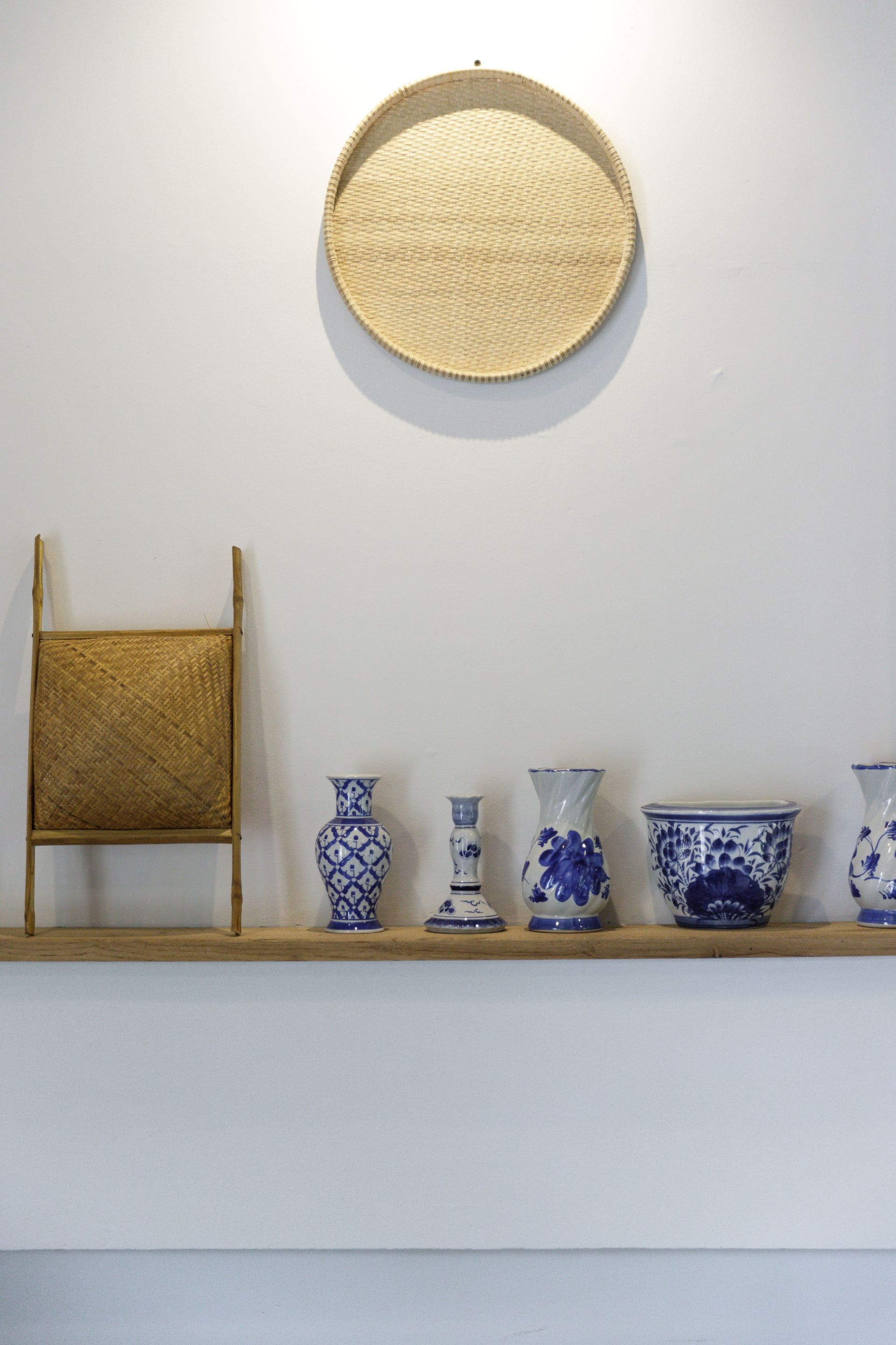 Um quarto com uma cadeira de fibra natural, um tapete redondo de fibra natural e uma prateleira com cinco vasos azuis e brancos.
