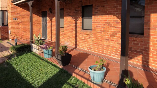 Un edificio de ladrillo con un patio cubierto, plantas en macetas y un pequeño jardín.