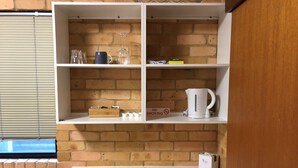 Una cocina con estantes blancos, una encimera blanca y una pared de ladrillo.
