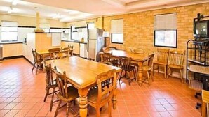 Un comedor amplio con una gran mesa de madera y sillas, una cocina al fondo y una pared de ladrillo.