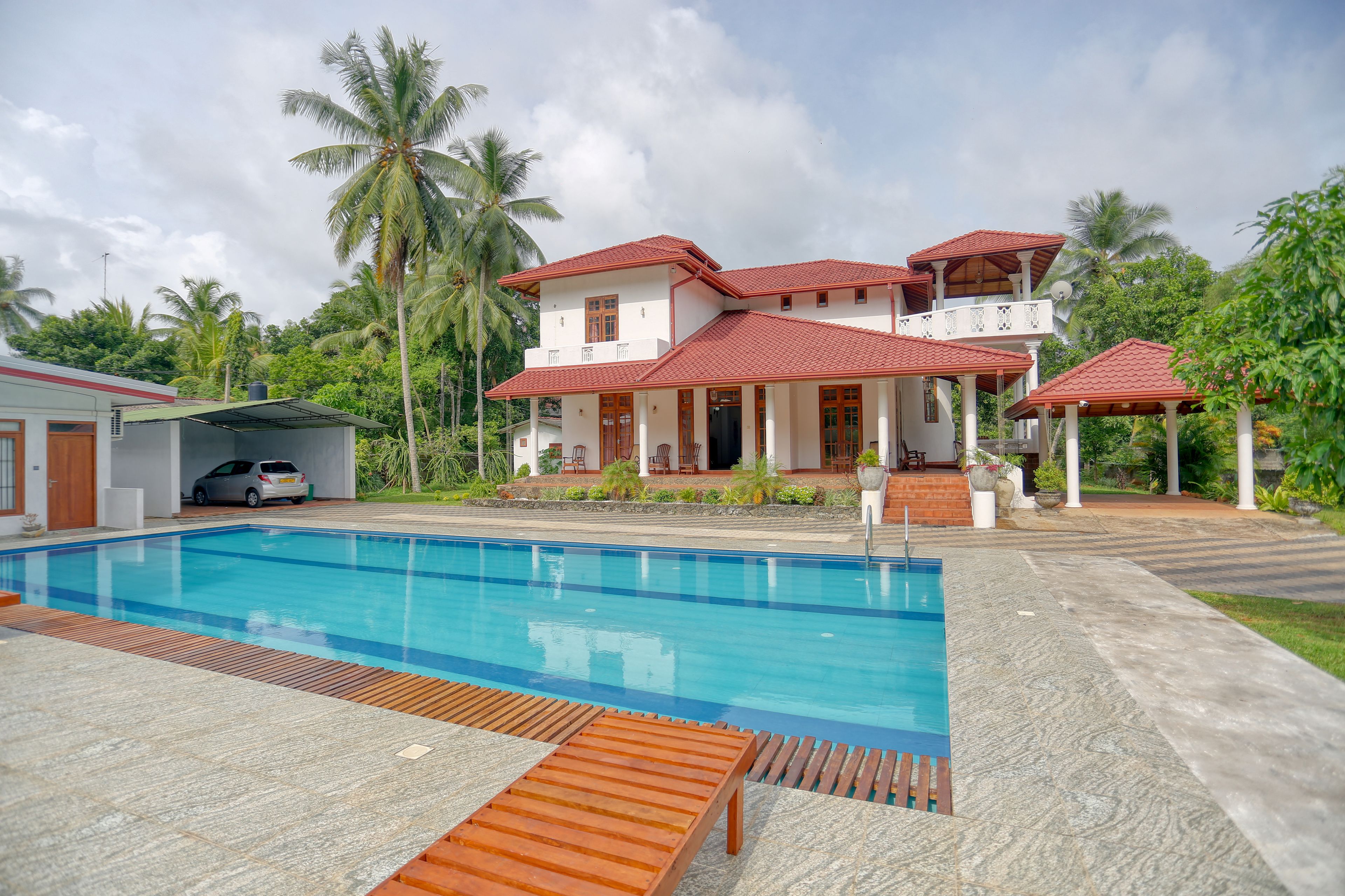 A two-story house with a swimming pool, a covered patio, and a car parked nearby.