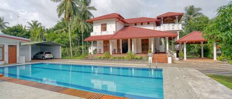 A two-story house with a swimming pool, a covered patio, and a car parked nearby.