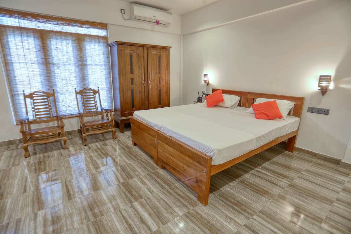 A bedroom with a large bed, wooden wardrobe, and two chairs.