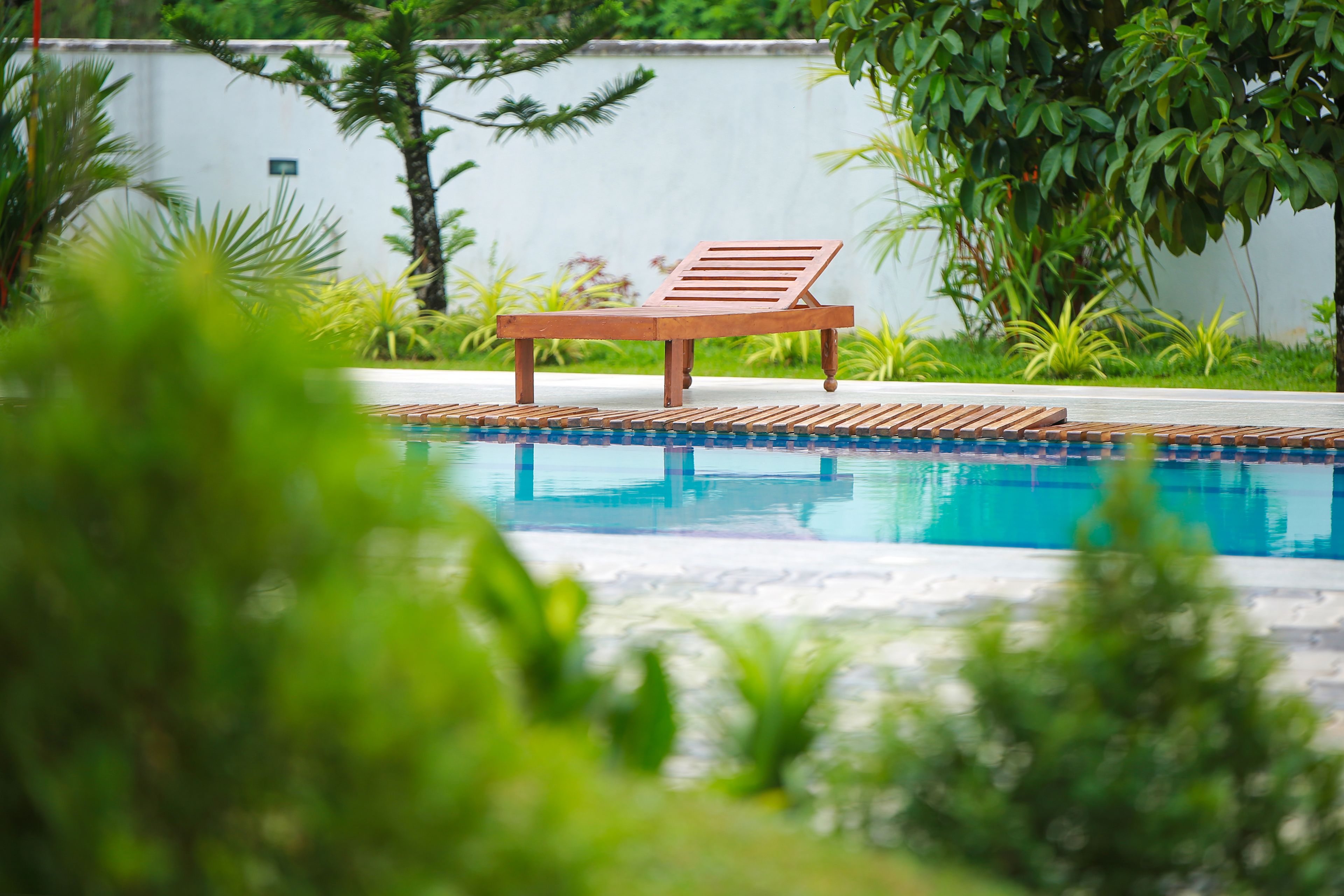 A poolside area with a wooden lounge chair and a pool.