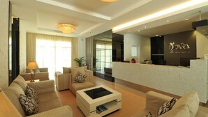Een moderne hotellobby met een receptiebalie, banken, een bijzettafeltje en een kroonluchter.