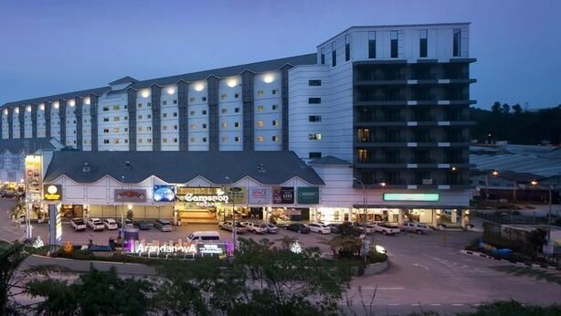 Een hotel met meerdere verdiepingen, een centraal atrium en een parkeerplaats ervoor.