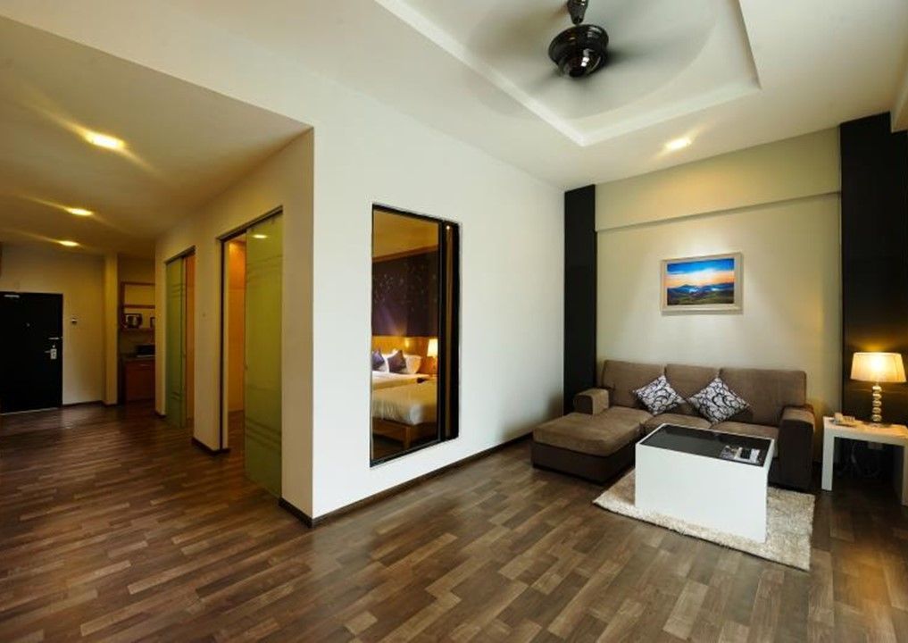 A modern hotel room with a wooden floor, a sofa, a coffee table, and a bed visible through a glass door.