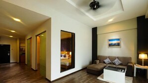 Een moderne hotelkamer met een houten vloer, een bank, een bijzettafeltje en een bed dat door een glazen deur zichtbaar is.