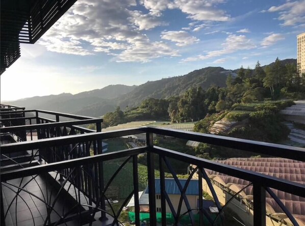 A balcony with a view of a river, mountains, and a building in the distance.