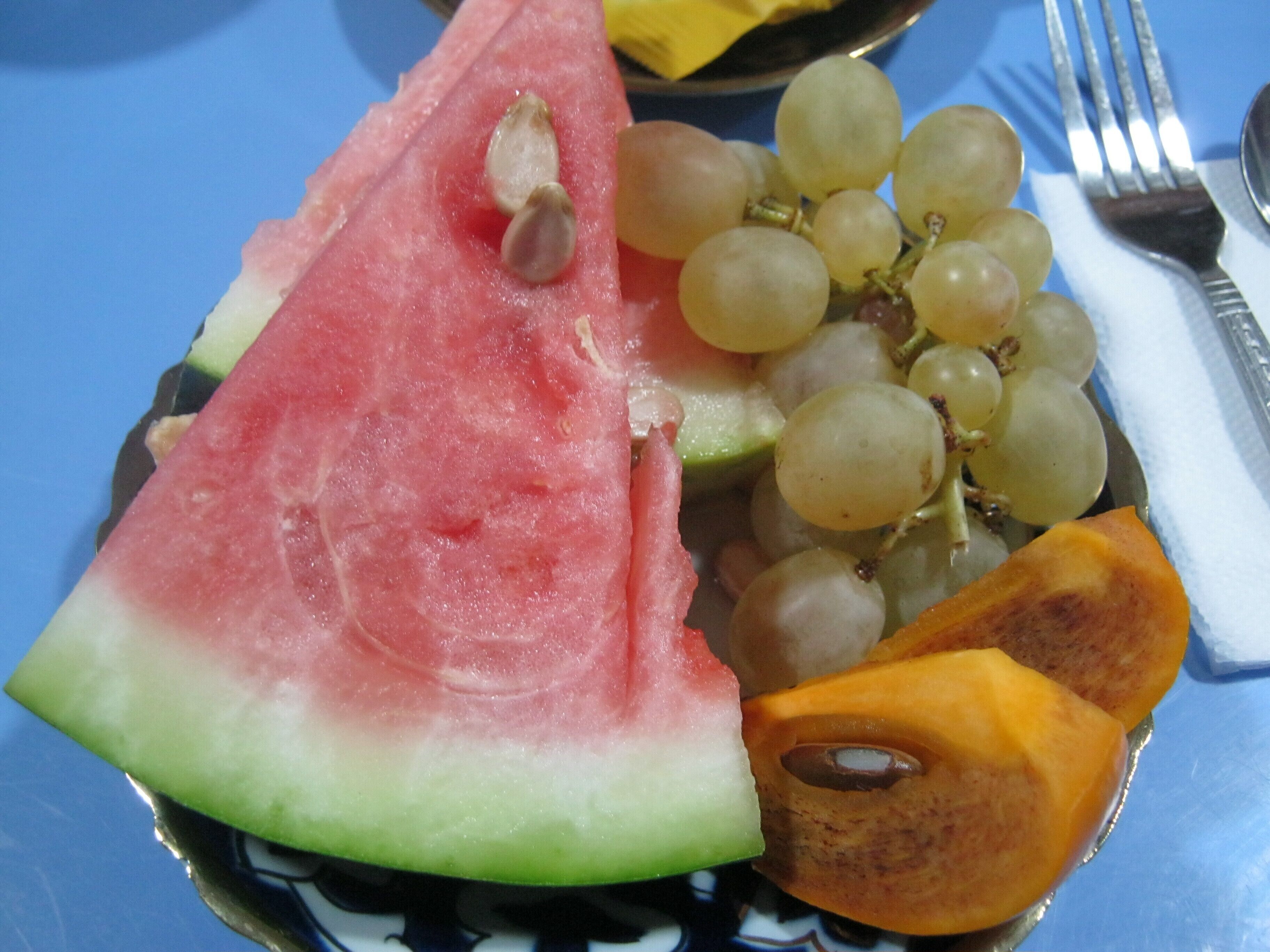 A plate with a slice of watermelon, a bunch of grapes, and a piece of orange fruit.