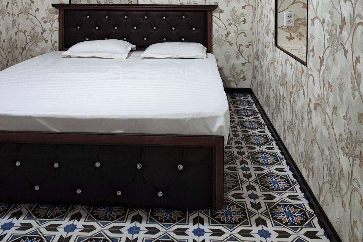 A bedroom with a bed, floral wallpaper, a decorative mirror, and patterned floor tiles.