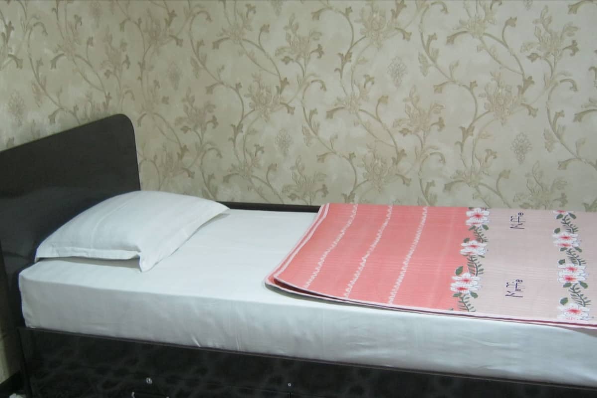 A single bed with a white sheet and a pink floral bedspread.