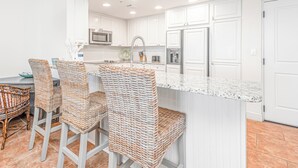 A kitchen with white cabinets, a stainless steel refrigerator, a microwave, and a bar area with wicker chairs.