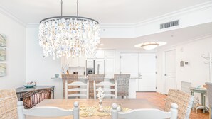 A dining room with a chandelier, white furniture, and a kitchen in the background.