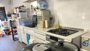 A kitchen with a gas stove, microwave, and various kitchen appliances. There is a water dispenser and a sink. - Yoko House (Uruma)