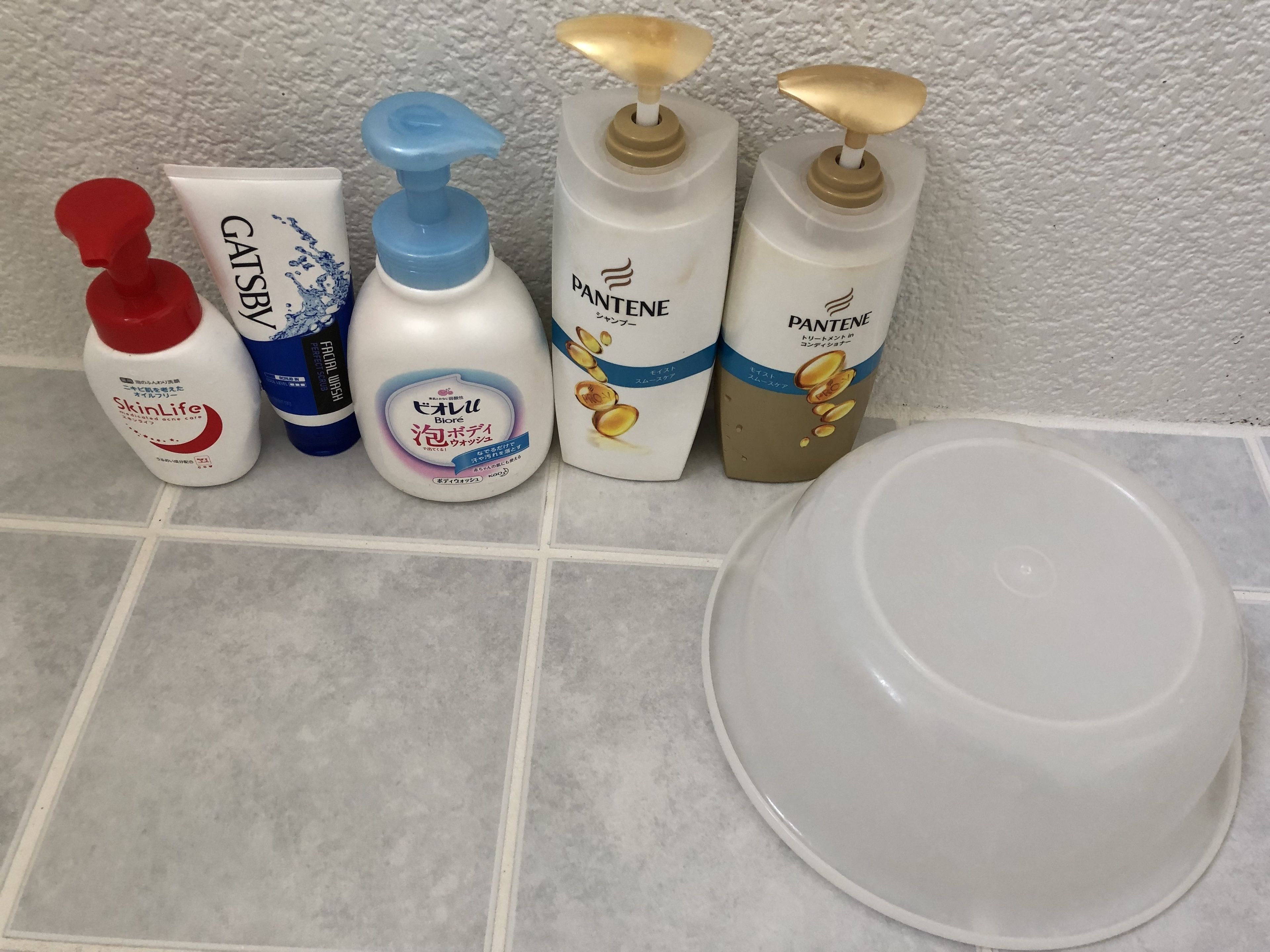 Una encimera de baño con cinco botellas de artículos de tocador y un lavabo blanco.