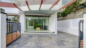 Uma entrada de prédio moderna com porta de vidro, portão de metal e área de pátio com azulejos.