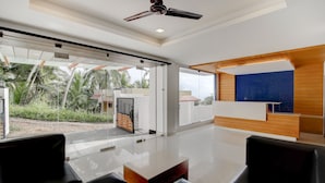 Uma área de recepção moderna com um balcão de madeira, uma janela ampla com vista para o verde e um ventilador de teto.