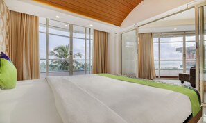 A modern hotel room with a large bed, large windows, and a view of palm trees. - Treebo Trend Cilantro By The Sea (Neyyattinkara)