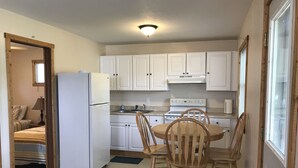 Una cocina compacta con armarios blancos, un refrigerador, una estufa y una mesa de comedor con sillas.