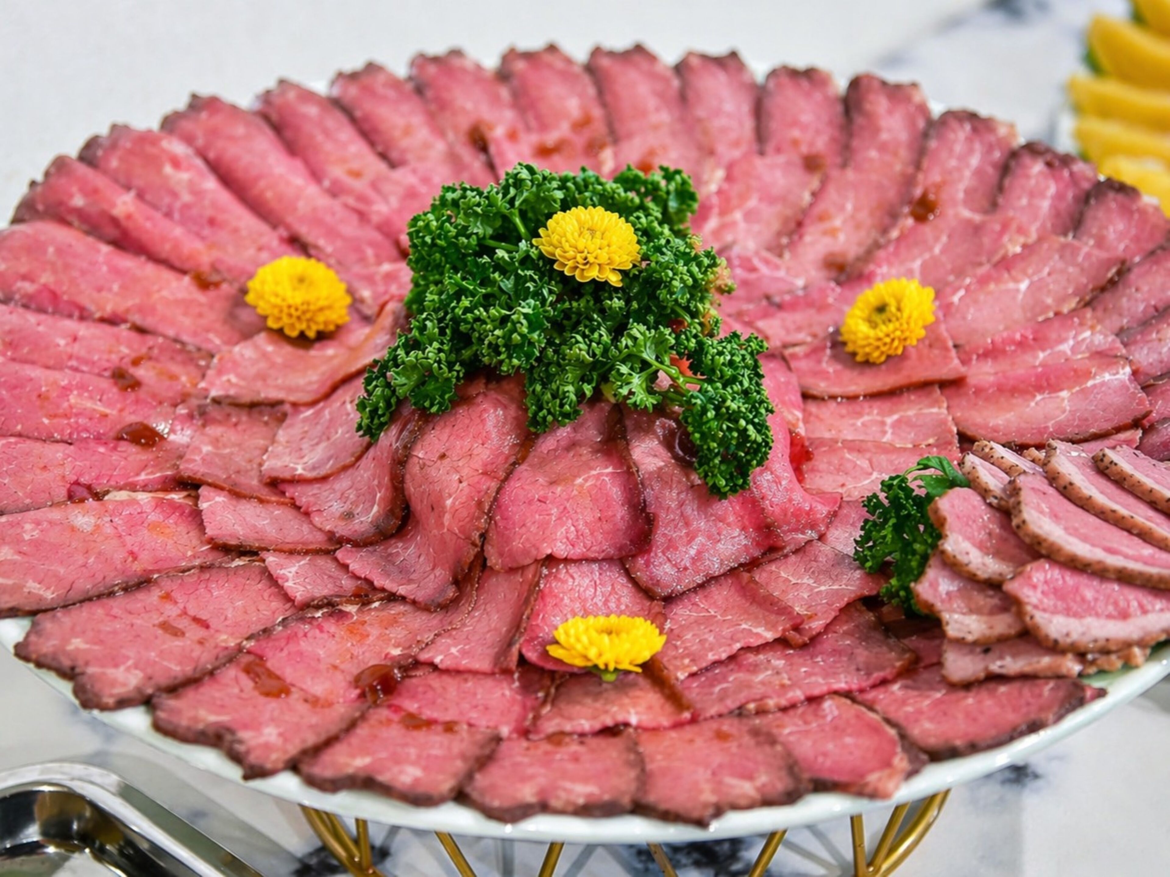 A round platter of sliced meat garnished with parsley and yellow flowers.