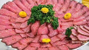 A round platter of sliced meat garnished with parsley and yellow flowers.