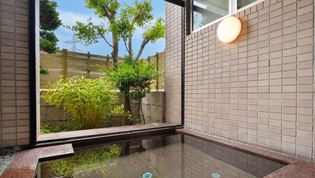 A modern interior with a glass-enclosed hot tub, a stone wall, and a wooden fence visible outside. - Chino Sky View Hotel (Chino)