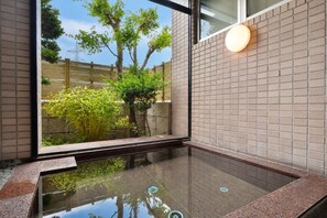 A modern interior with a glass-enclosed hot tub, a stone wall, and a wooden fence visible outside. - Chino Sky View Hotel (Chino)