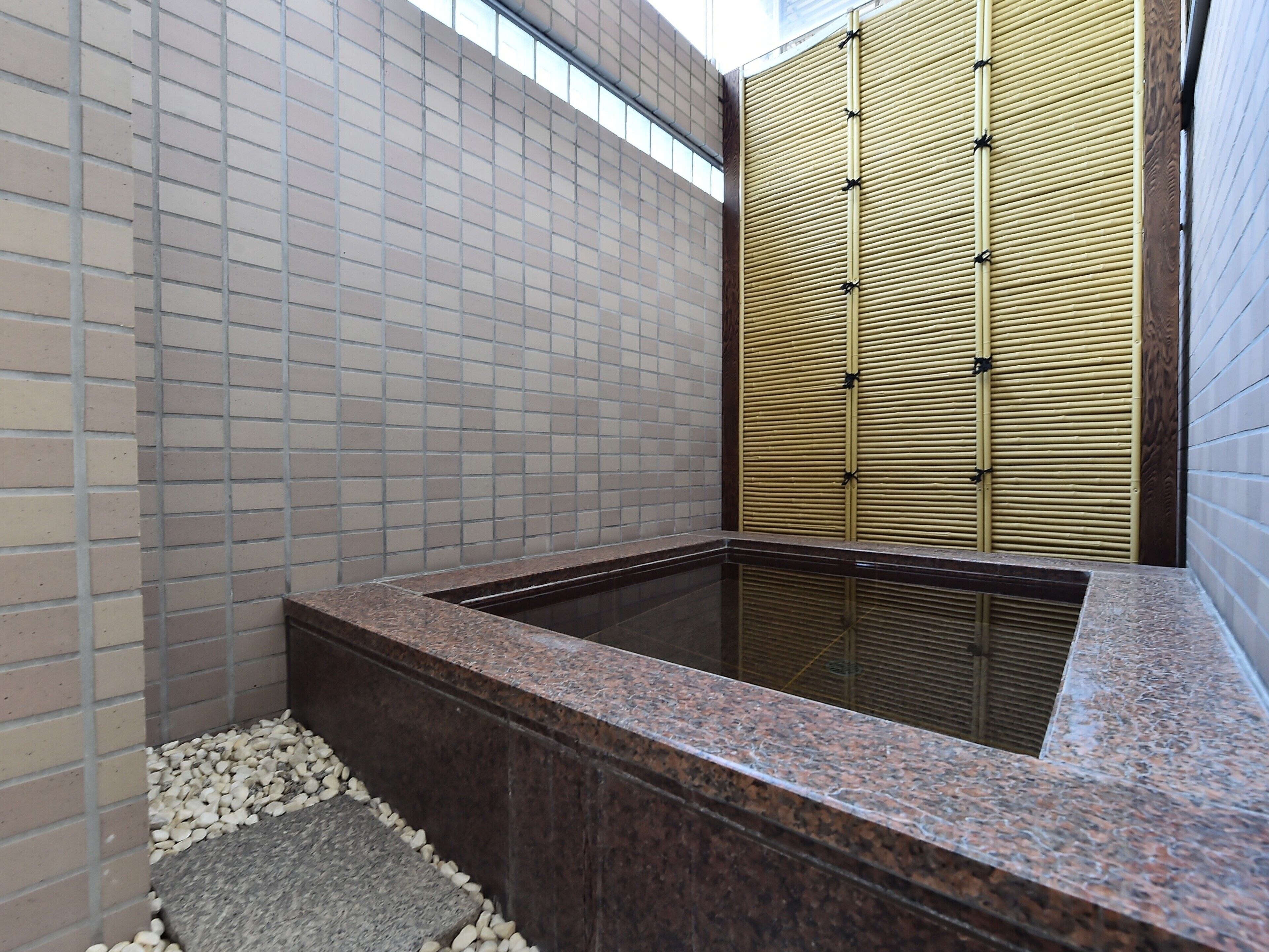 Un área de spa con un jacuzzi, paredes con azulejos y una mampara de bambú.