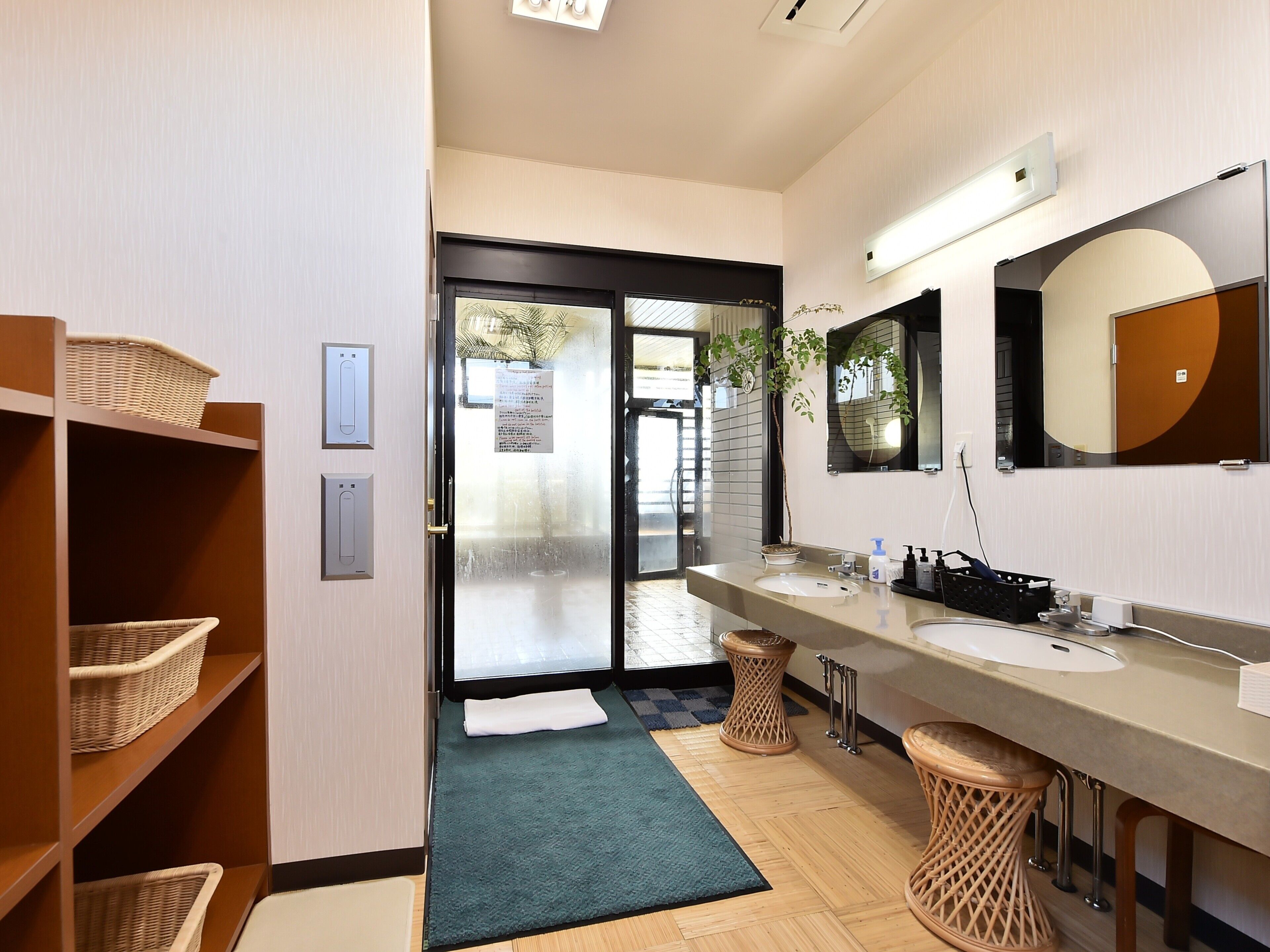 A modern bathroom with two sinks, a large mirror, and wicker baskets on shelves.