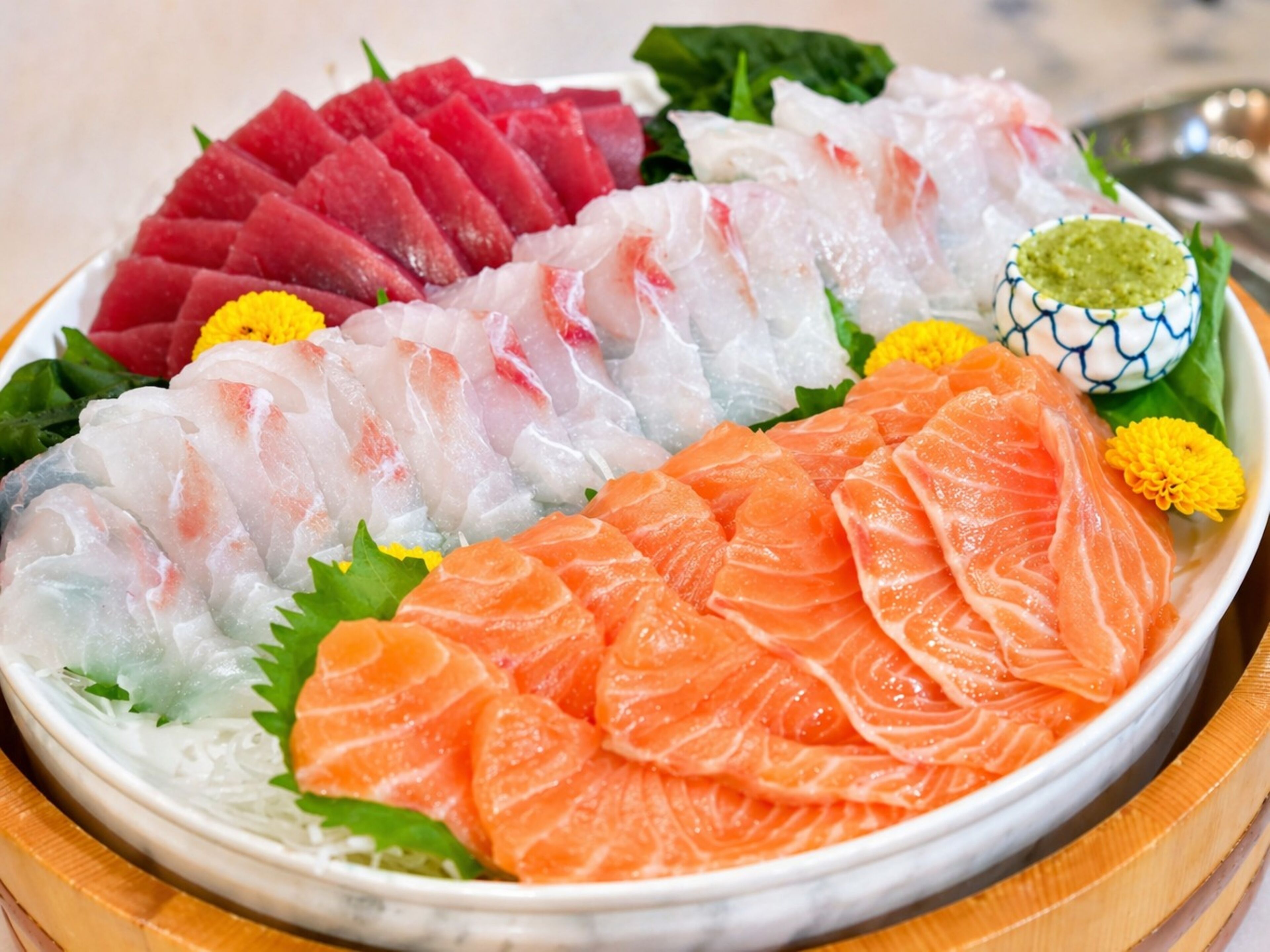 A plate of sashimi with various types of fish, garnished with green leaves and flowers.