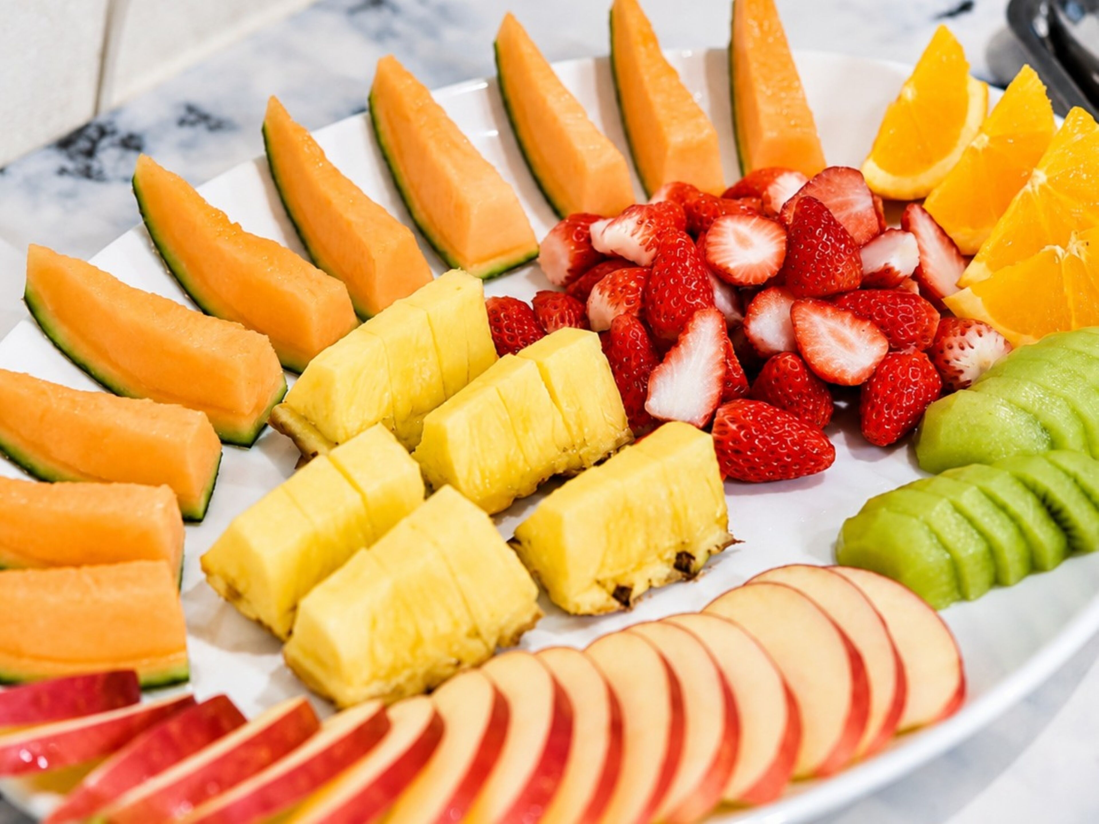 A plate of assorted fruits including cantaloupe, pineapple, strawberries, kiwi, and apple slices.