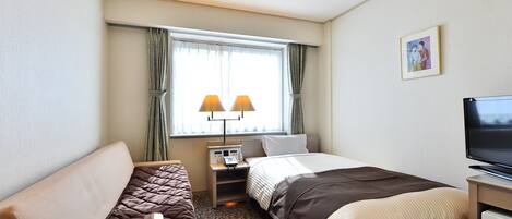 Habitación de hotel con cama, sofá, escritorio con lámpara, televisión y ventana con cortinas.