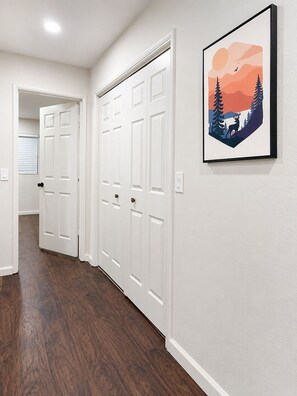 Ein Flur mit weißen Türen, einem gerahmten Bild an der Wand und Holzboden.