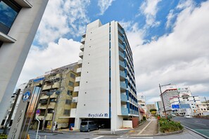 Um hotel com vários andares, com um letreiro chamativo 'BaySide', um estacionamento e vista para a rua com outros edifícios.