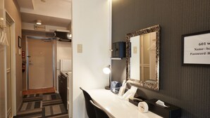 Habitación de hotel con escritorio, silla, espejo y un cartel con el número de habitación y los servicios.