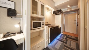 Una kitchenette compacta con microondas, estufa y lavamanos. Hay un pequeño escritorio con una lámpara y un certificado enmarcado en la pared.
